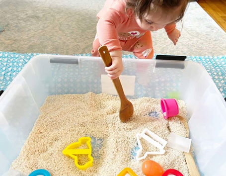 girl digging in sand box with spoon